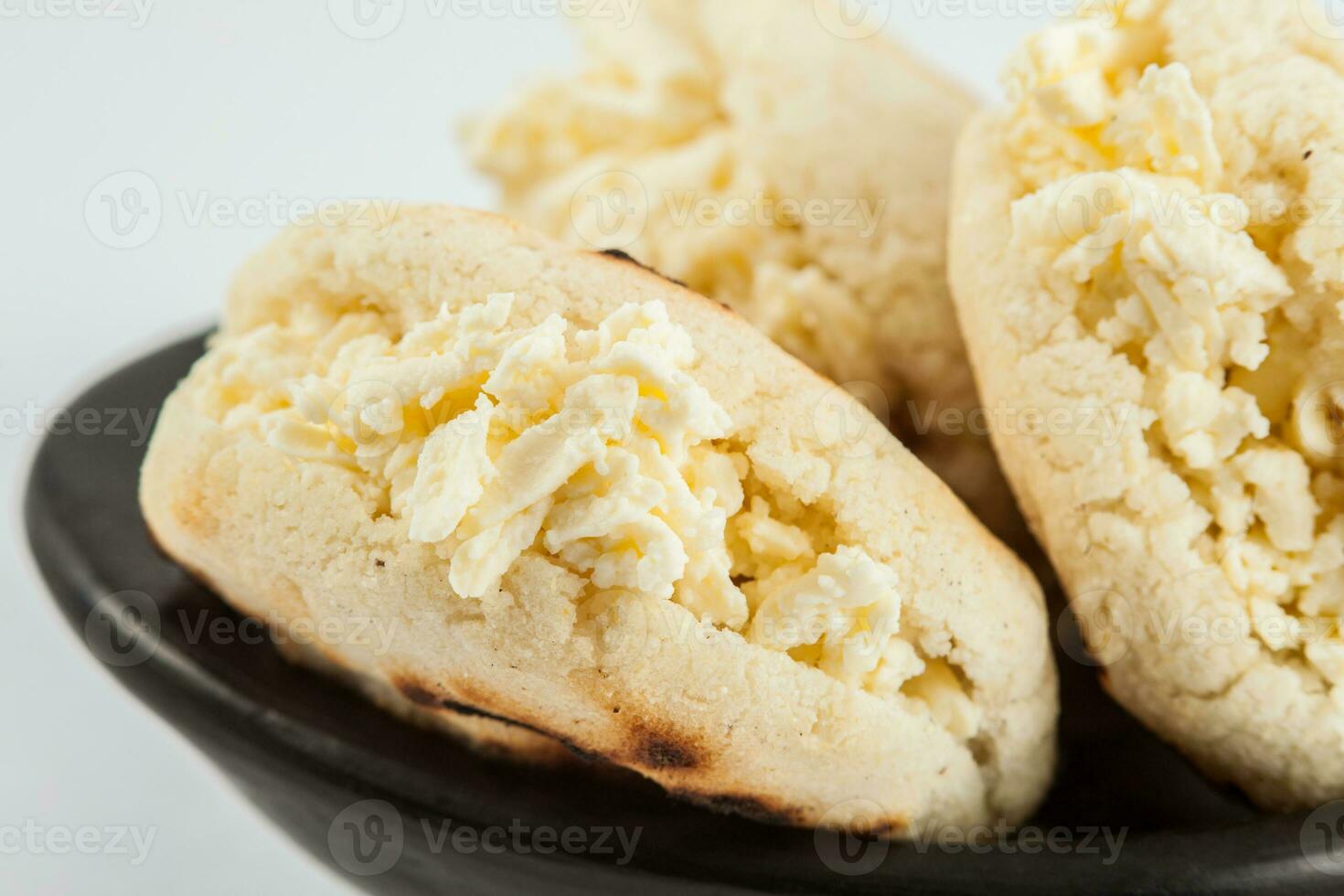 Colombian traditional white corn arepa stuffed with grated cheese in a black ceramic dish on white background photo