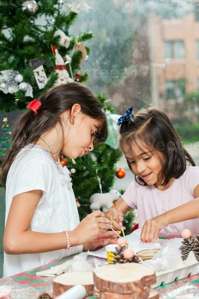 dos pequeño hermanas teniendo divertido mientras haciendo Navidad natividad artesanía con a hogar - real familia foto