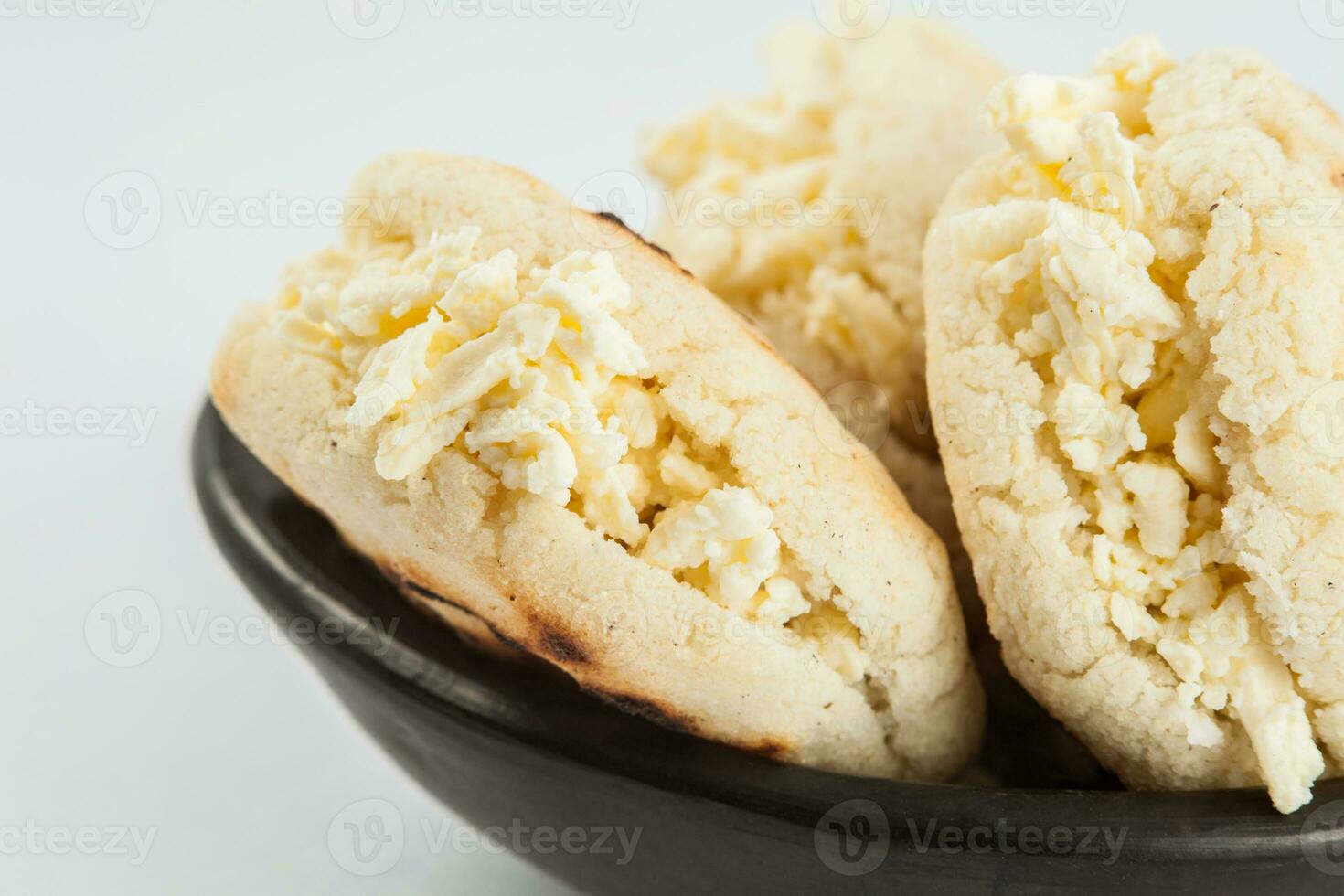 Colombian traditional white corn arepa stuffed with grated cheese in a black ceramic dish on white background photo