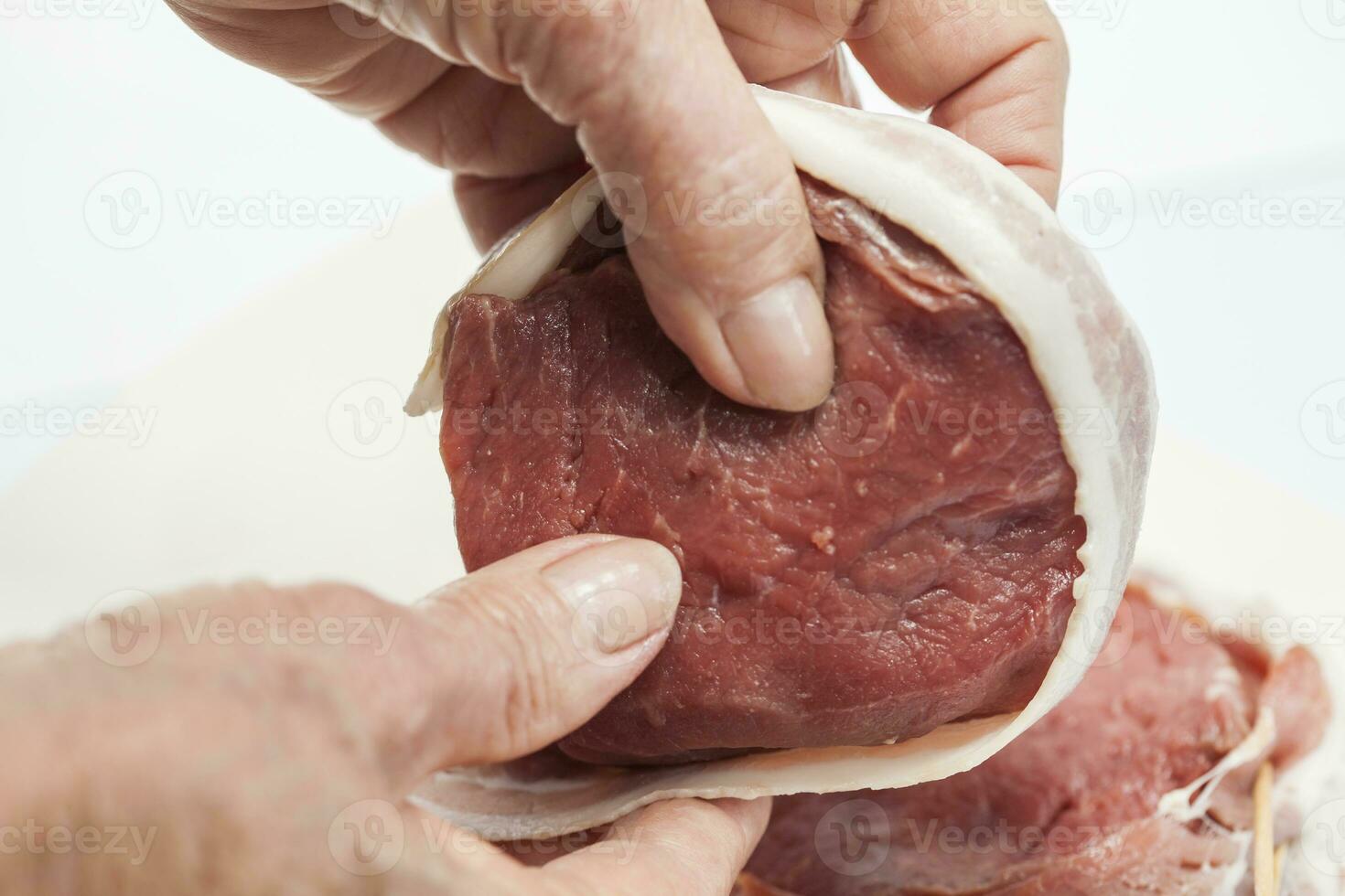 Wrapping beef tenderloin medallion with pork bacon. Filet mignon photo