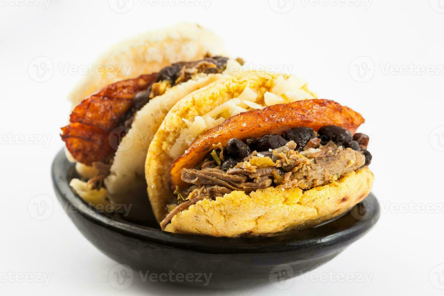 arepas lleno con triturado carne de res, negro frijoles, plátano y queso servido en un blanco plato en blanco antecedentes foto