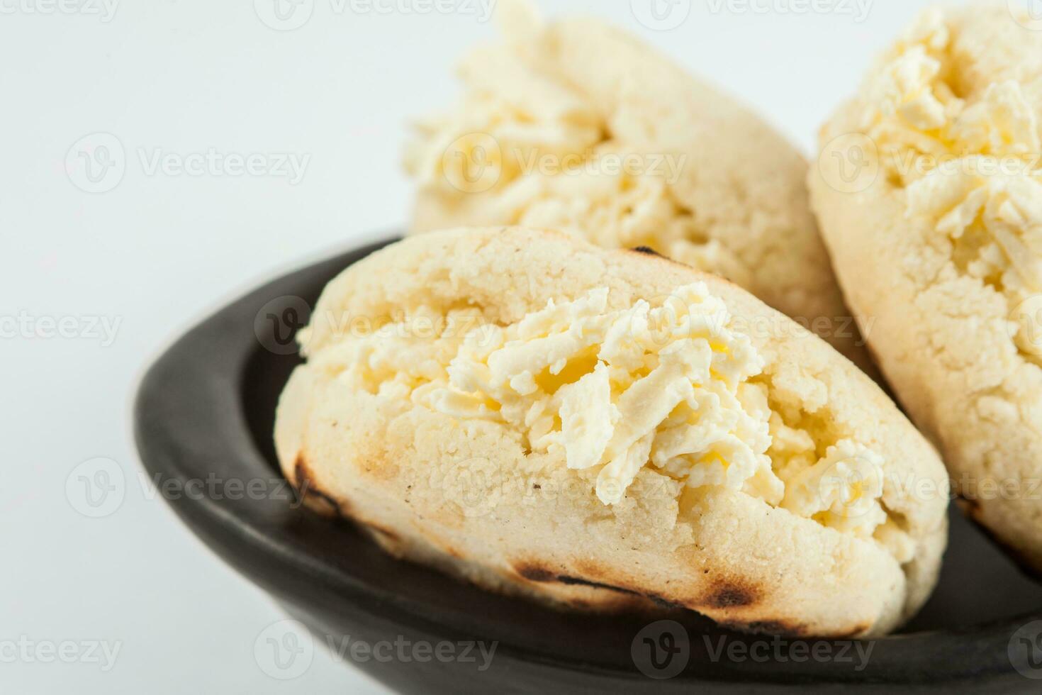 Colombian traditional white corn arepa stuffed with grated cheese in a black ceramic dish on white background photo