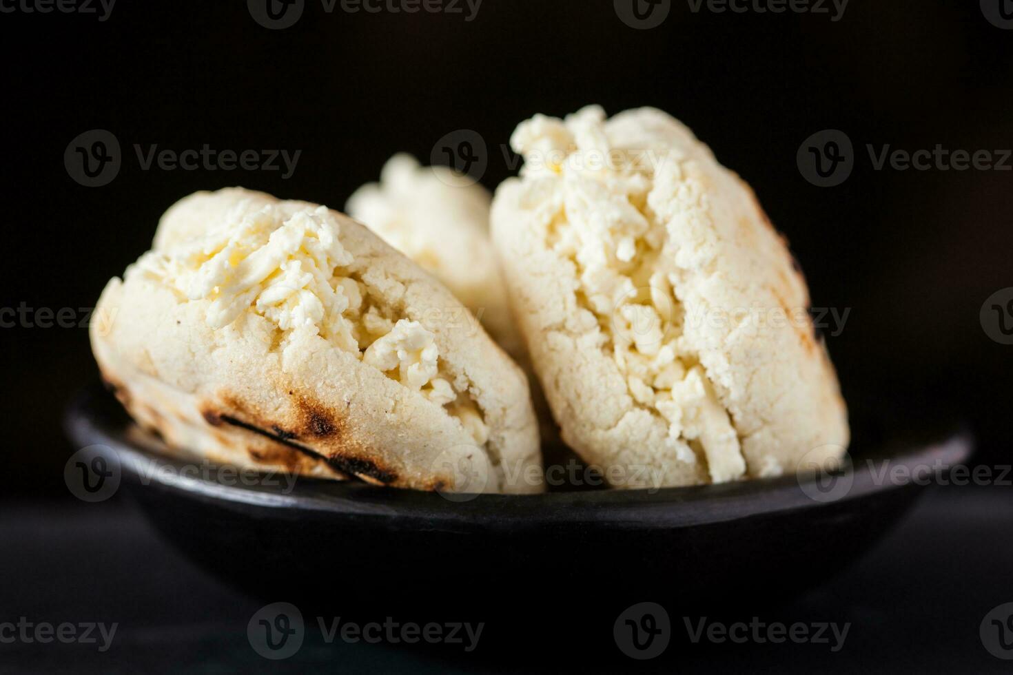 Colombian traditional white corn arepa stuffed with grated cheese in a black ceramic dish on black background photo