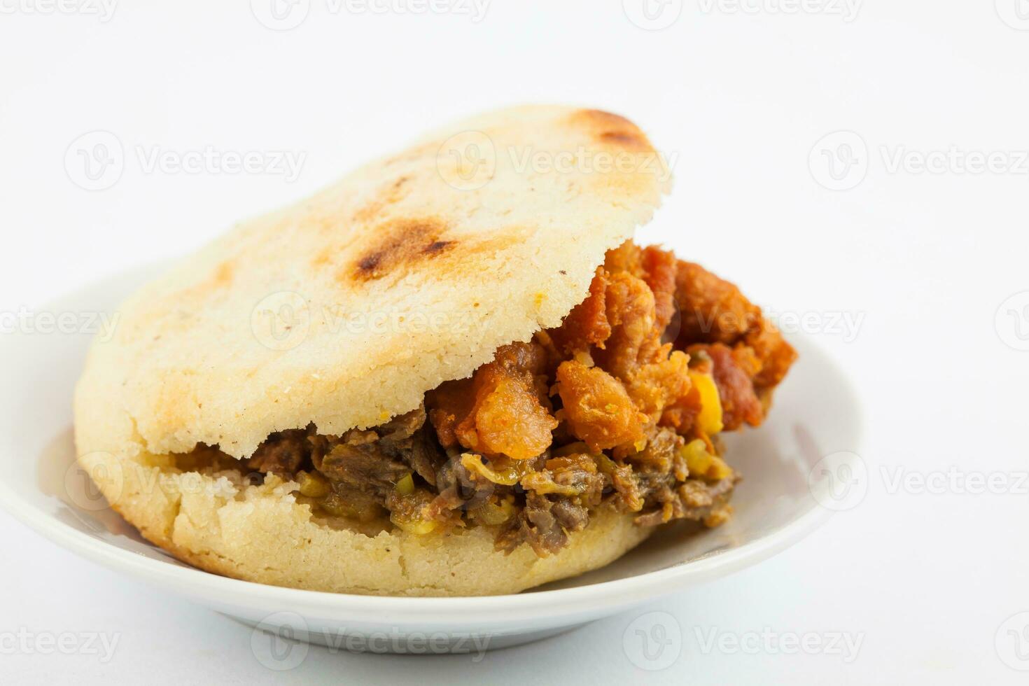 Arepas filled with shredded beef and pork rind served in white dish on white background photo