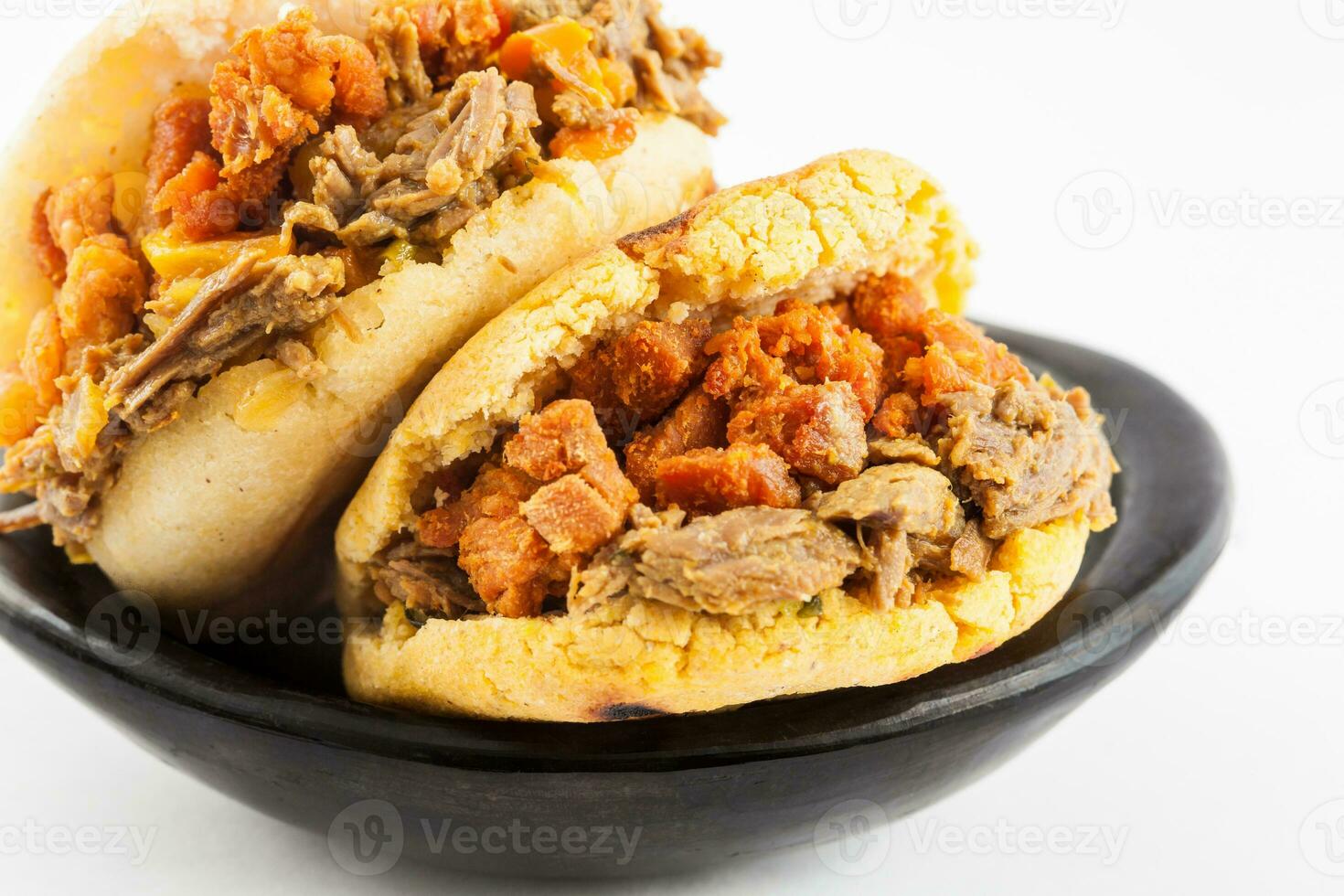 Arepas filled with shredded beef and pork rind served in a black ceramic dish on white background photo