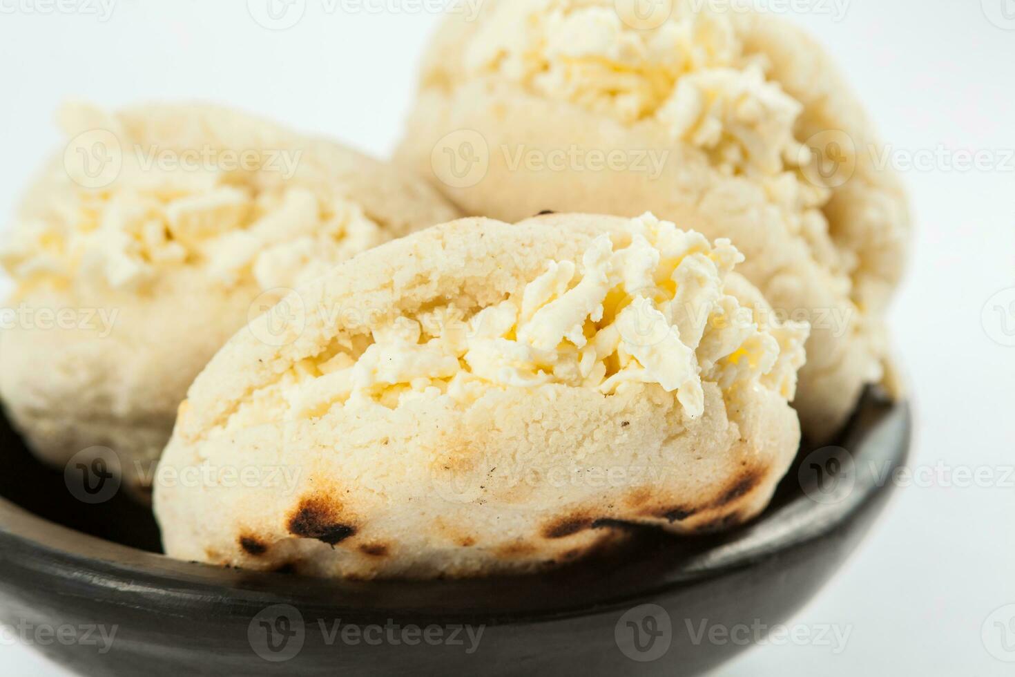 Colombiana tradicional blanco maíz arepa relleno con rallado queso en un negro cerámico plato en blanco antecedentes foto