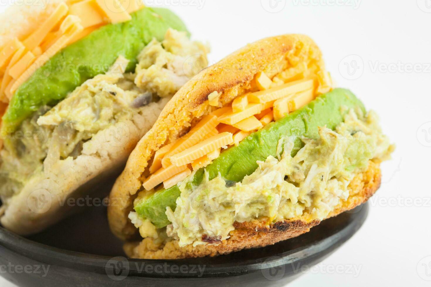 Arepas filled with shredded chicken and avocado served in a black ceramic dish on white background photo