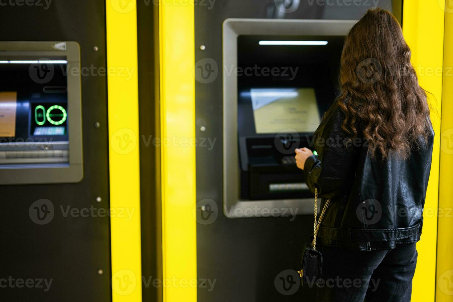 espalda de joven morena niña retirarse dinero desde crédito tarjeta a amarillo Cajero automático. foto