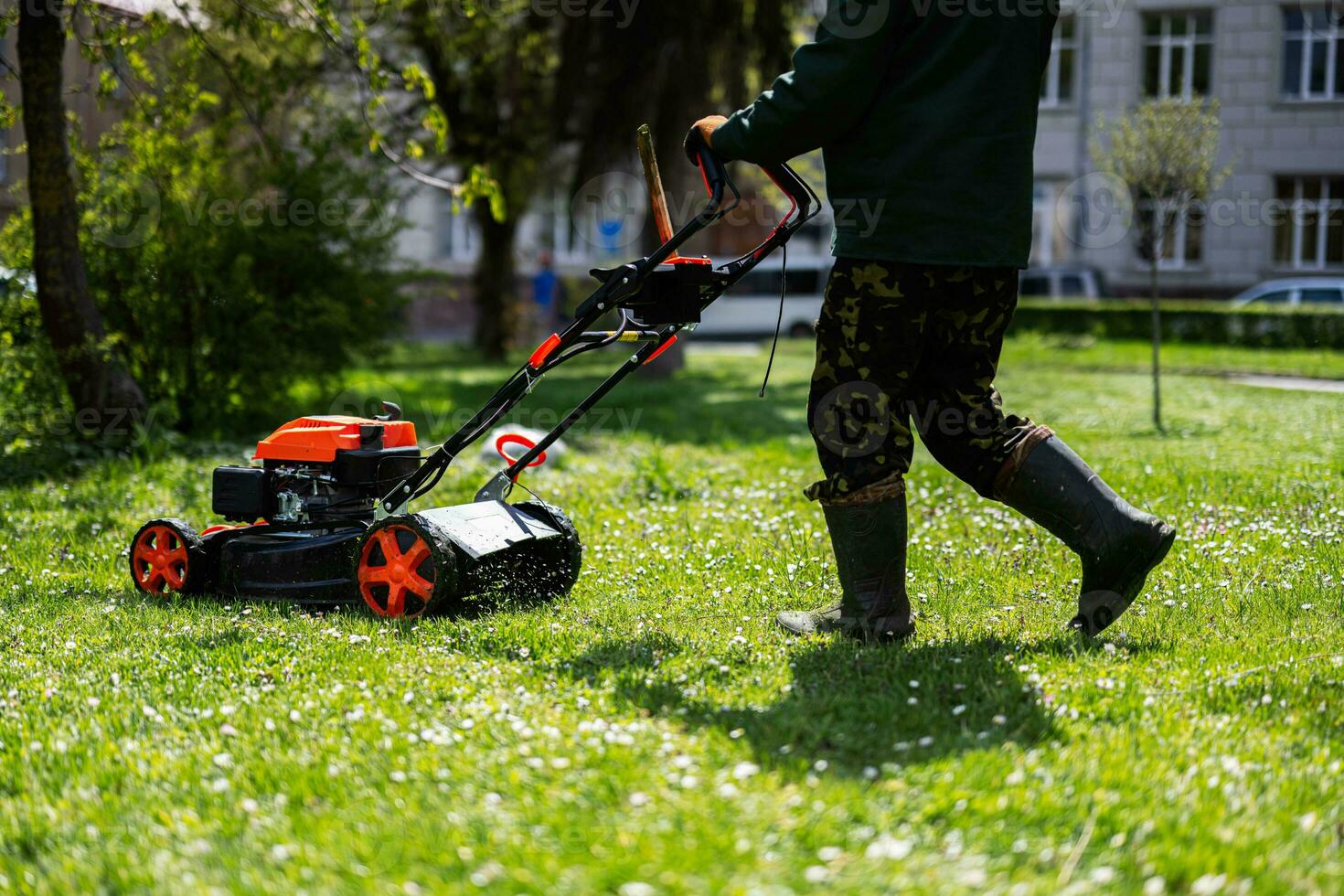 Communal services gardener worker man using lawn mower for grass cutting in city park. photo