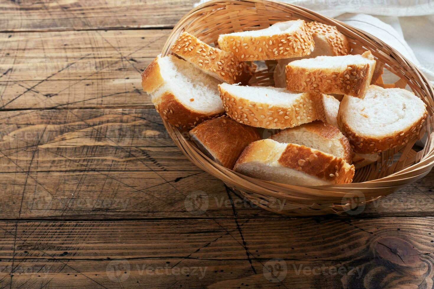 Fresh white bread, baguette slices in a wicker basket. Wooden rustic table background. Copy space photo