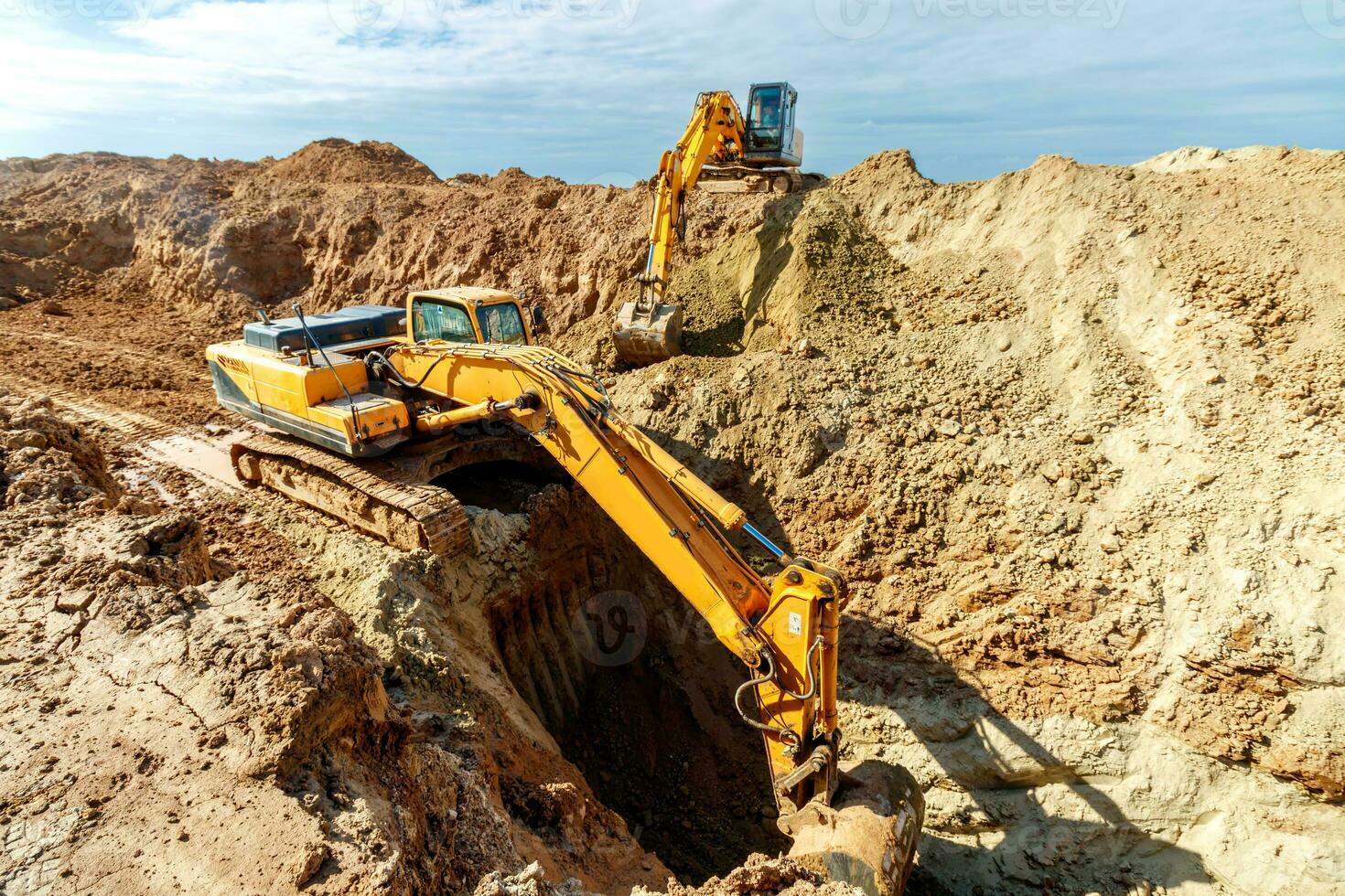 Two Excavator are digging soil in the construction site on sky background,with white fluffy cloud photo