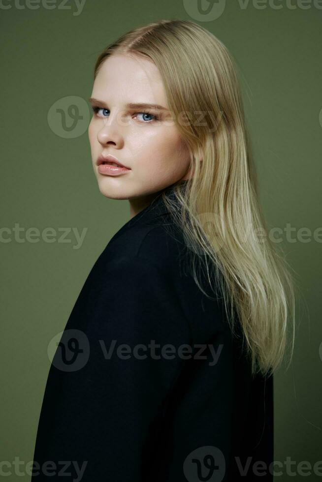 A beautiful girl looks half-turned into the camera at you posing on a green background in a jacket in the studio photo