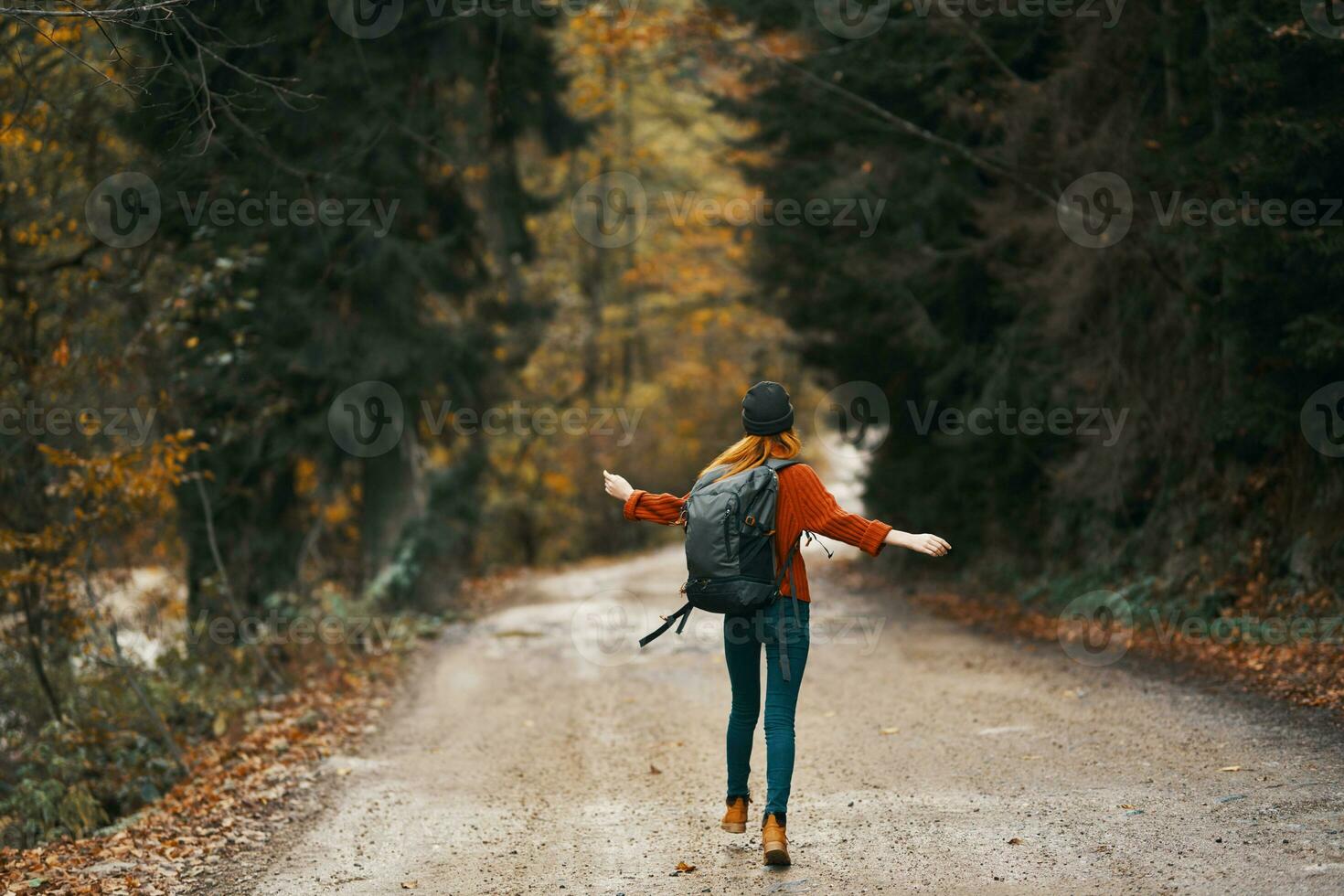 mujer en pantalones chaqueta con un mochila camina a lo largo el la carretera en el otoño bosque foto