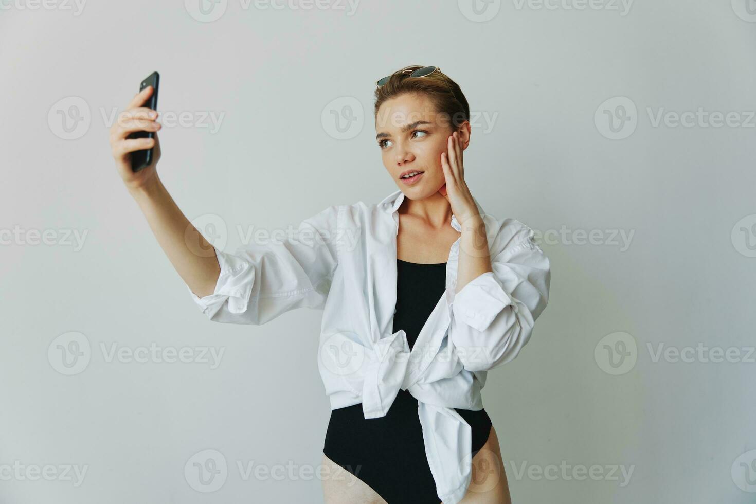 Teenage girl blogger takes photos and shoots. herself on video on her phone for social media content, video blogger, selfies against a white wall with a smile at home, freelancer