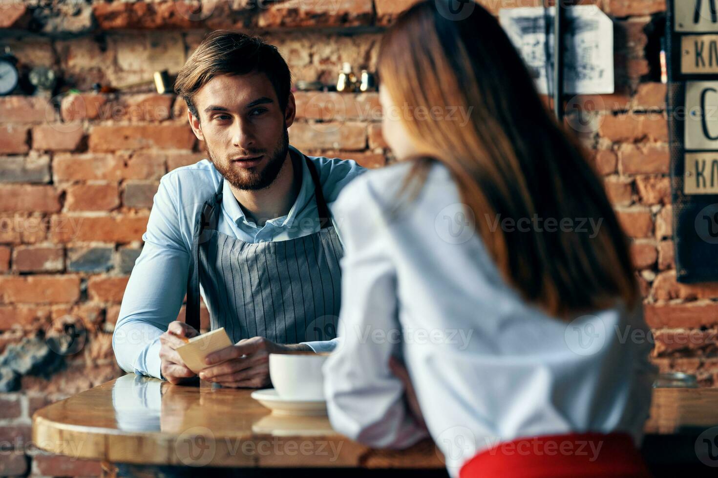 a man with a cup of coffee and all aprons at a cafe table and a woman in a shirt and red skirt cropped view photo