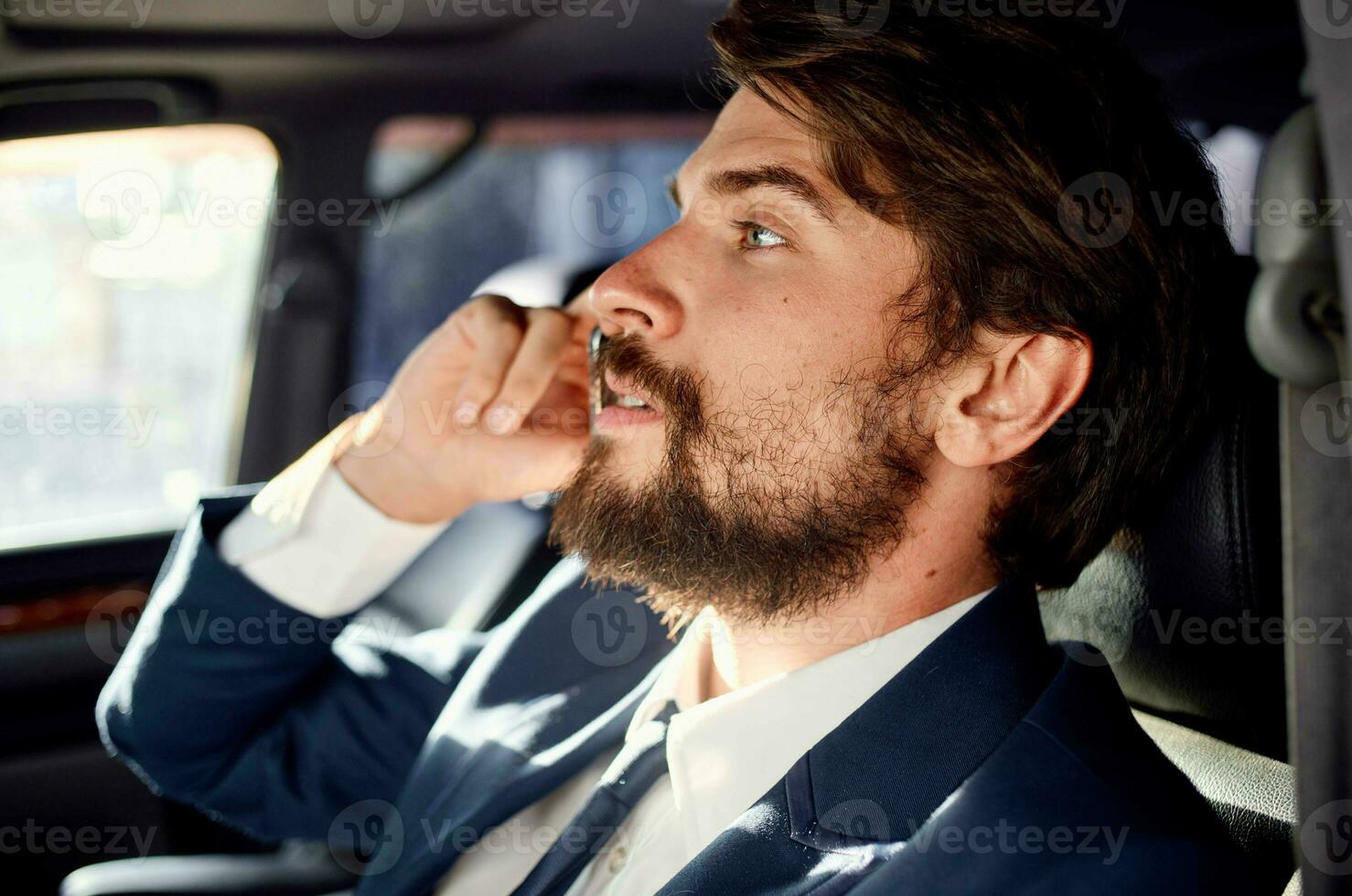 a man in a suit is sitting in the car and talking on the phone photo