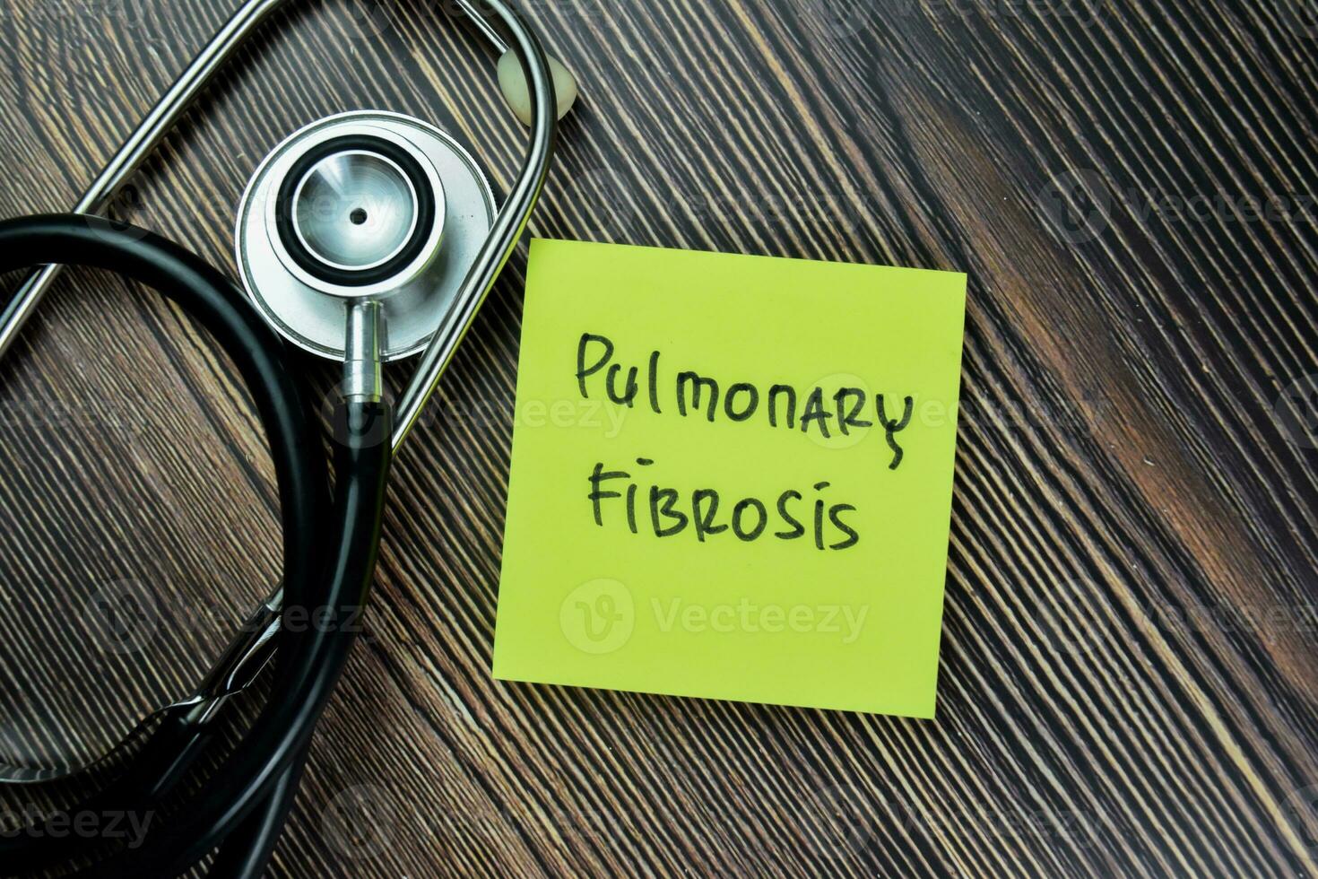 Concept of Pulmonary Fibrosis write on sticky notes with stethoscope isolated on Wooden Table. photo