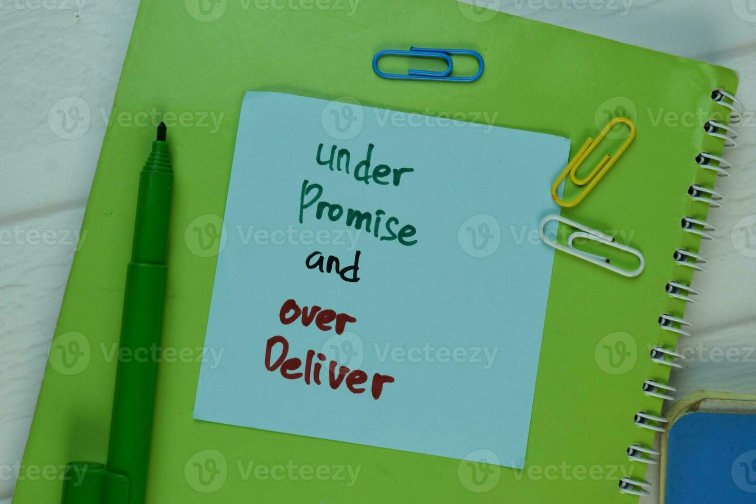 Under Promise and Over Deliver write on sticky note isolated on Wooden Table. photo