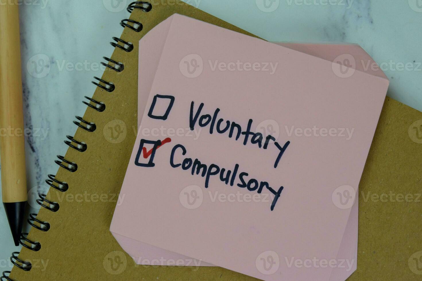 Concept of Voluntary or Compulsory write on sticky notes isolated on Wooden Table. photo