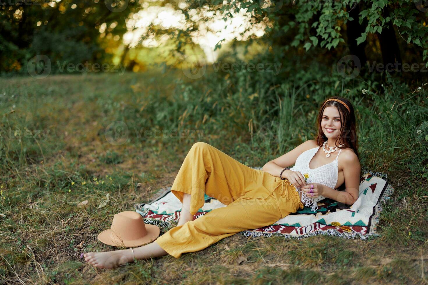 Young beautiful hippie woman lying on the ground in nature in the fall in eco clothes in yellow pants in the sunset light photo