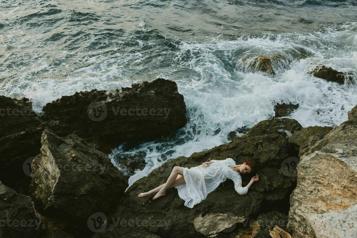 Barefoot woman in a white dress lying on a stone in a white dress unaltered photo