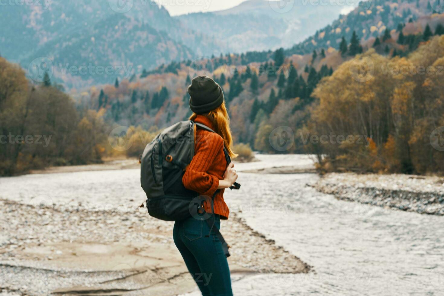woman in sweater with a backpack rest in the mountains near the river in autumn in nature and tall trees model photo