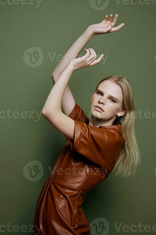 Professional blonde young female model in brown trendy dress holding hands up serious looks at camera curving dancing posing isolated on over olive green studio wall background. Seasonal sale banner photo