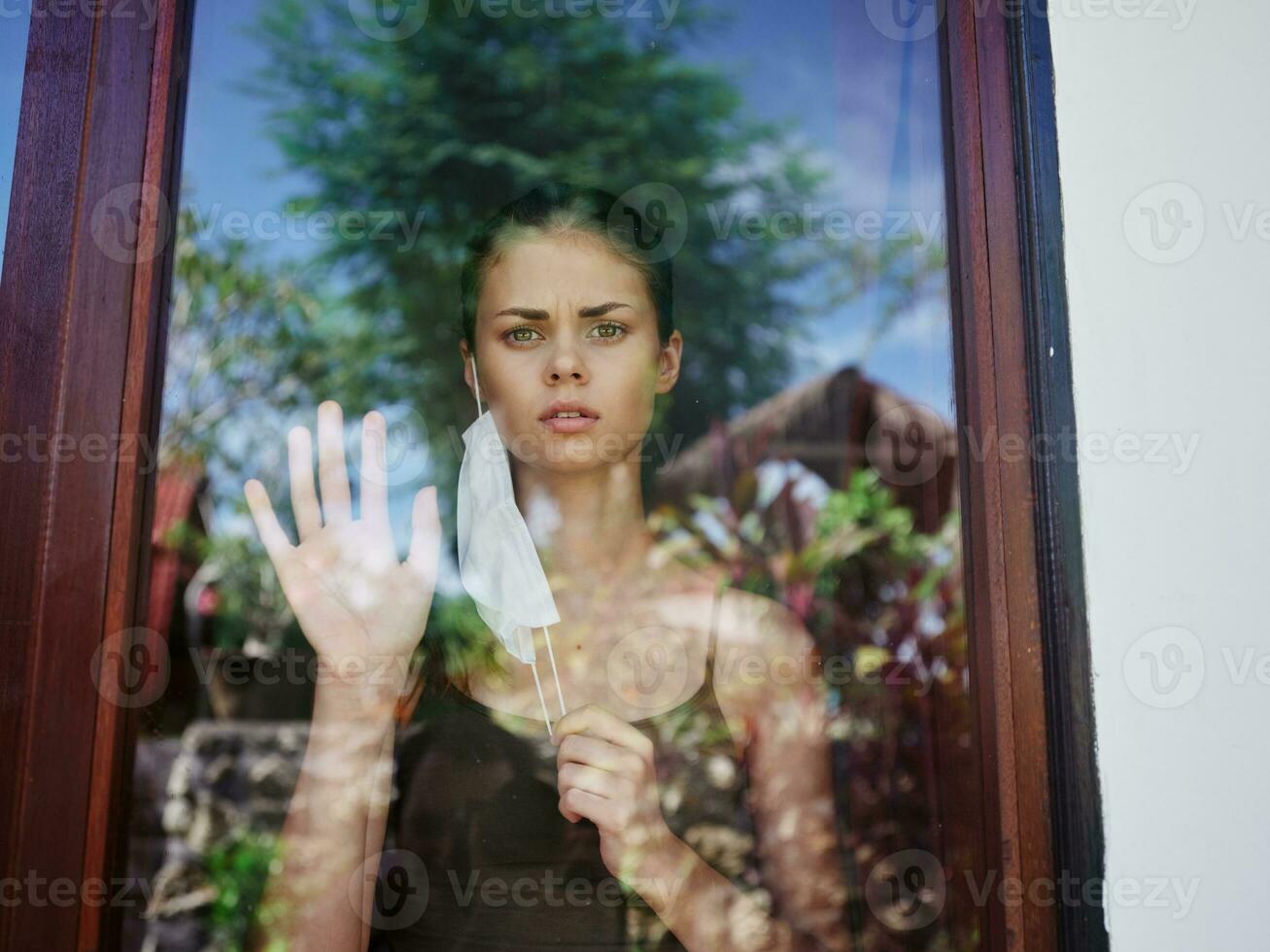 masked woman looking out the window lockdown quarantine photo