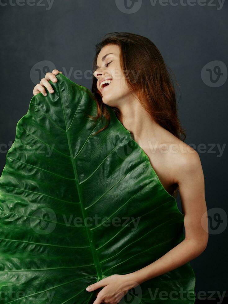 alegre bonito mujer cubre desnudo cuerpo con verde hoja foto