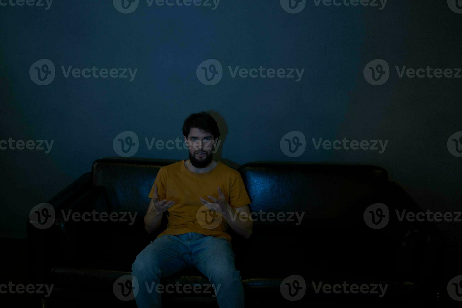 A man sits on a sofa indoors and watches TV front view photo