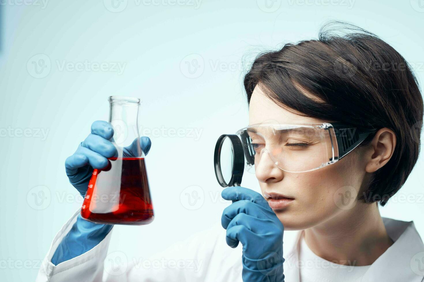 female laboratory assistant looks through a magnifying glass at a biochemical research process photo