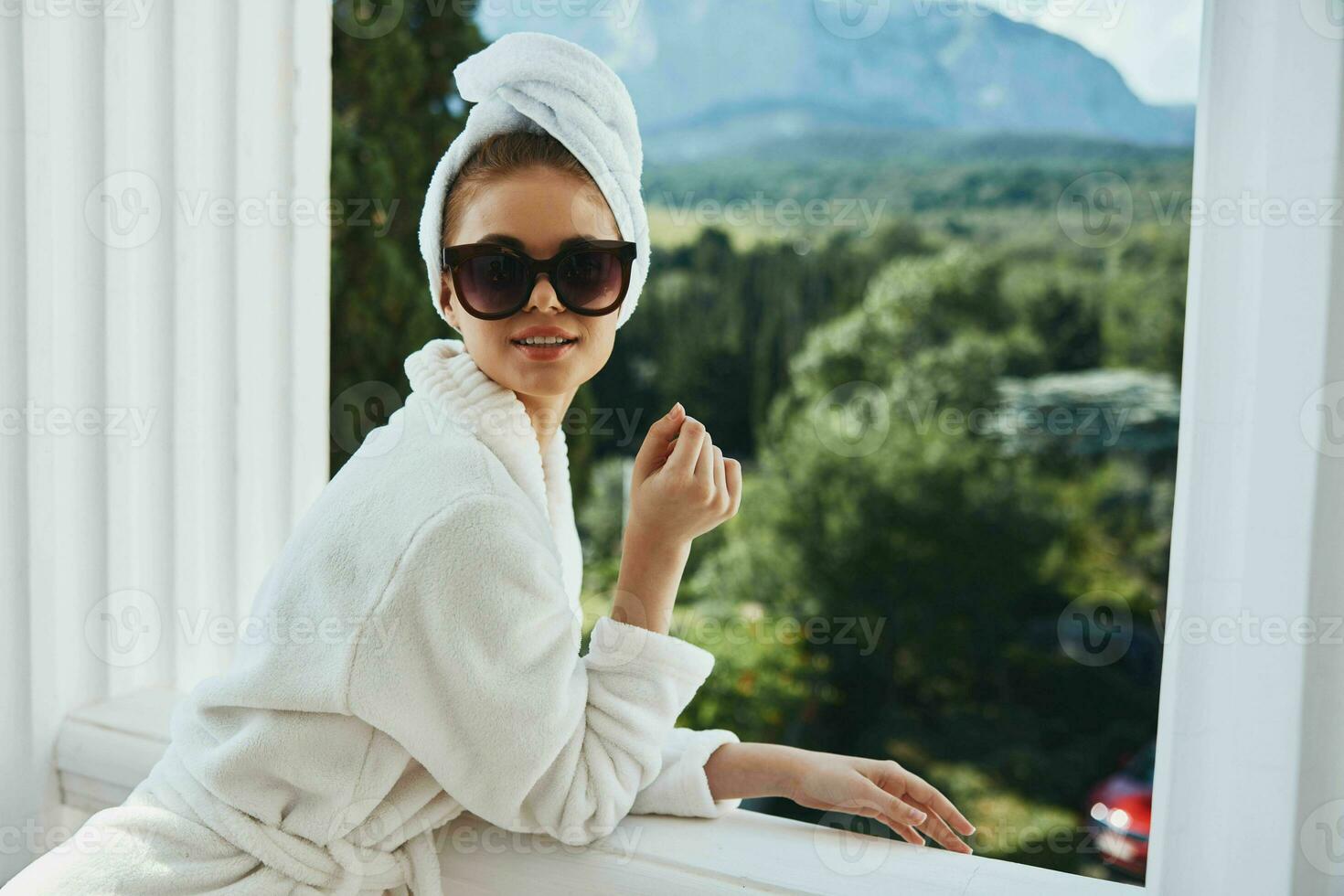 Portrait of gorgeous woman wearing sunglasses posing in a bathrobe on a balcony rest unaltered photo
