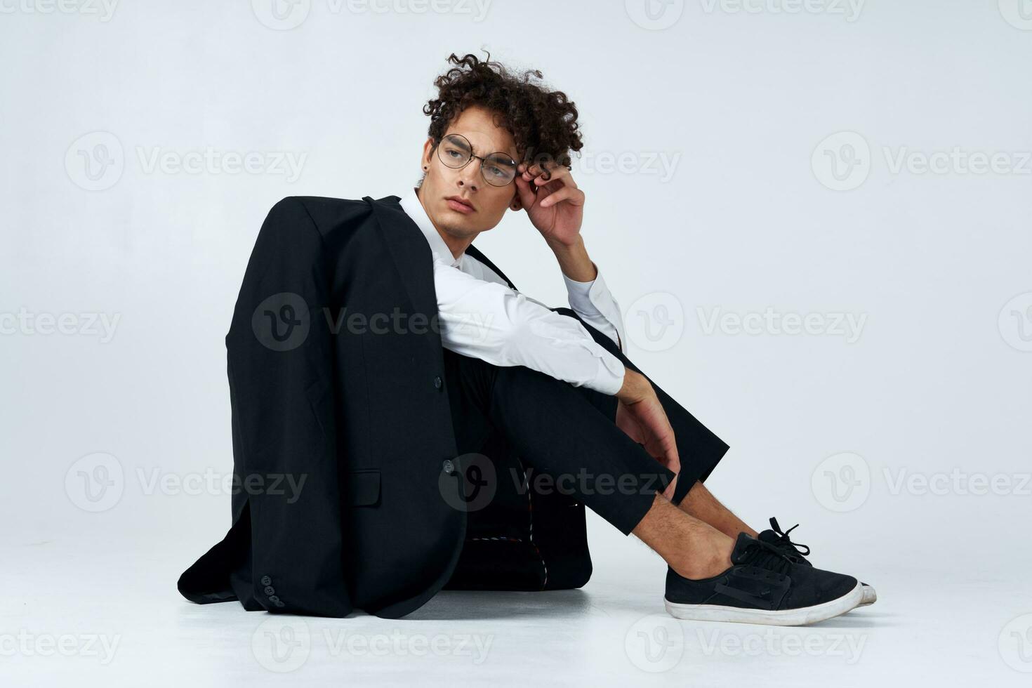 de moda chico con Rizado pelo en un clásico traje y zapatillas en el piso adentro fotografía estudio foto