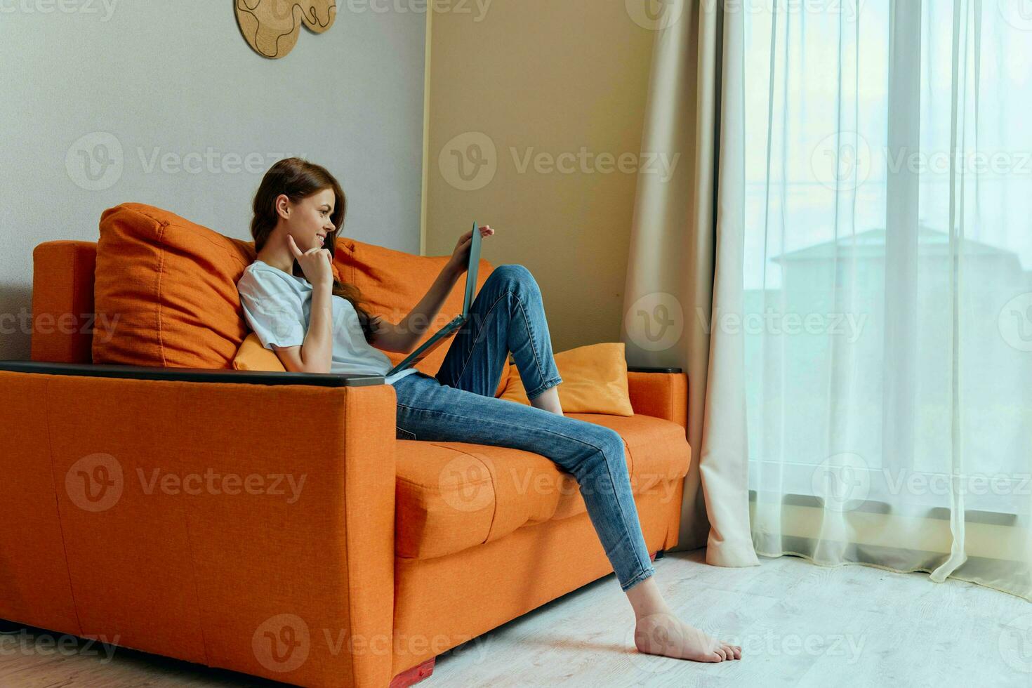 smiling woman chatting on the orange couch with a laptop unaltered photo