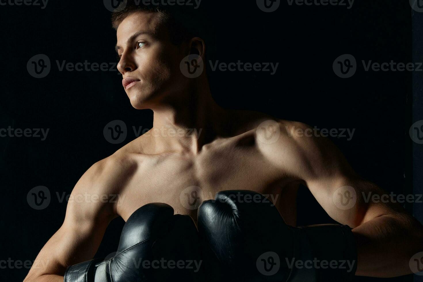 muscular boxer in black gloves on a dark background looking to the side photo