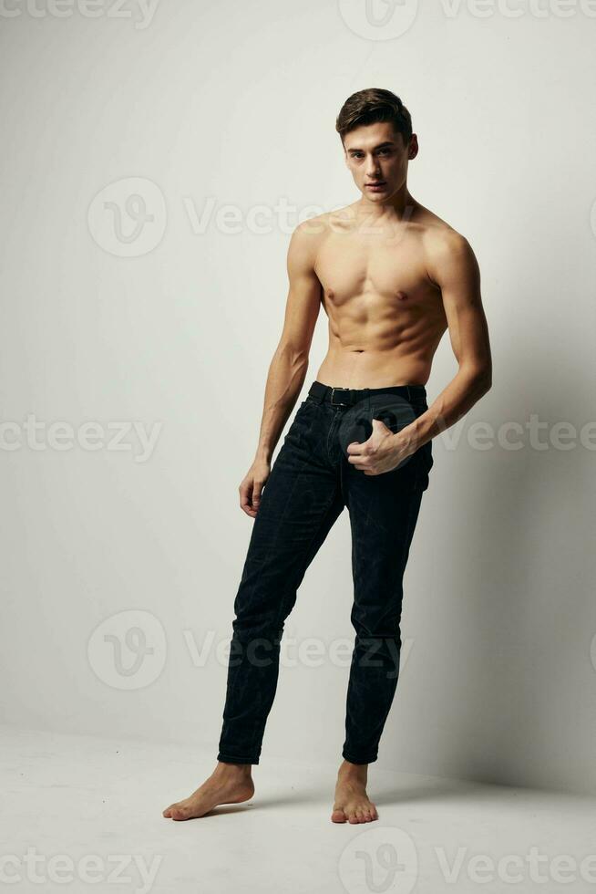 A sexy guy with a naked torso and in trousers is standing barefoot on the floor in a room photo