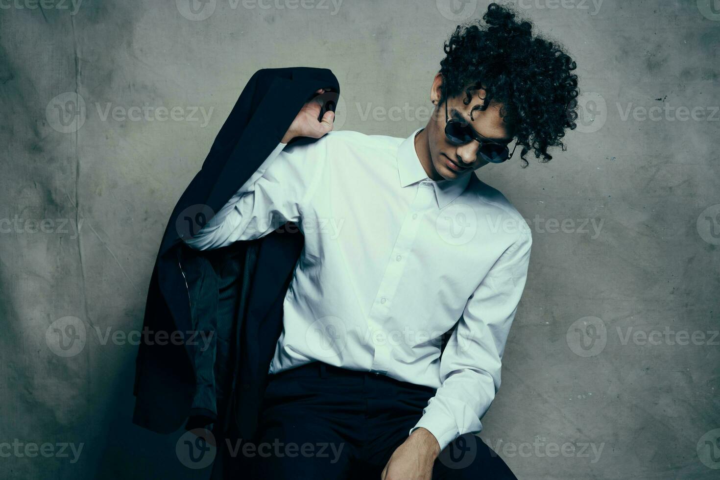 elegante chico en un traje se sienta en un silla adentro y lentes en su cara foto