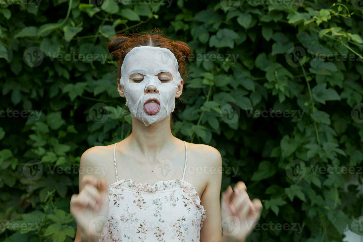 Portrait of a girl cosmetic maskc Shows his tongue and gestures with his hands osmetology bushes in the background photo