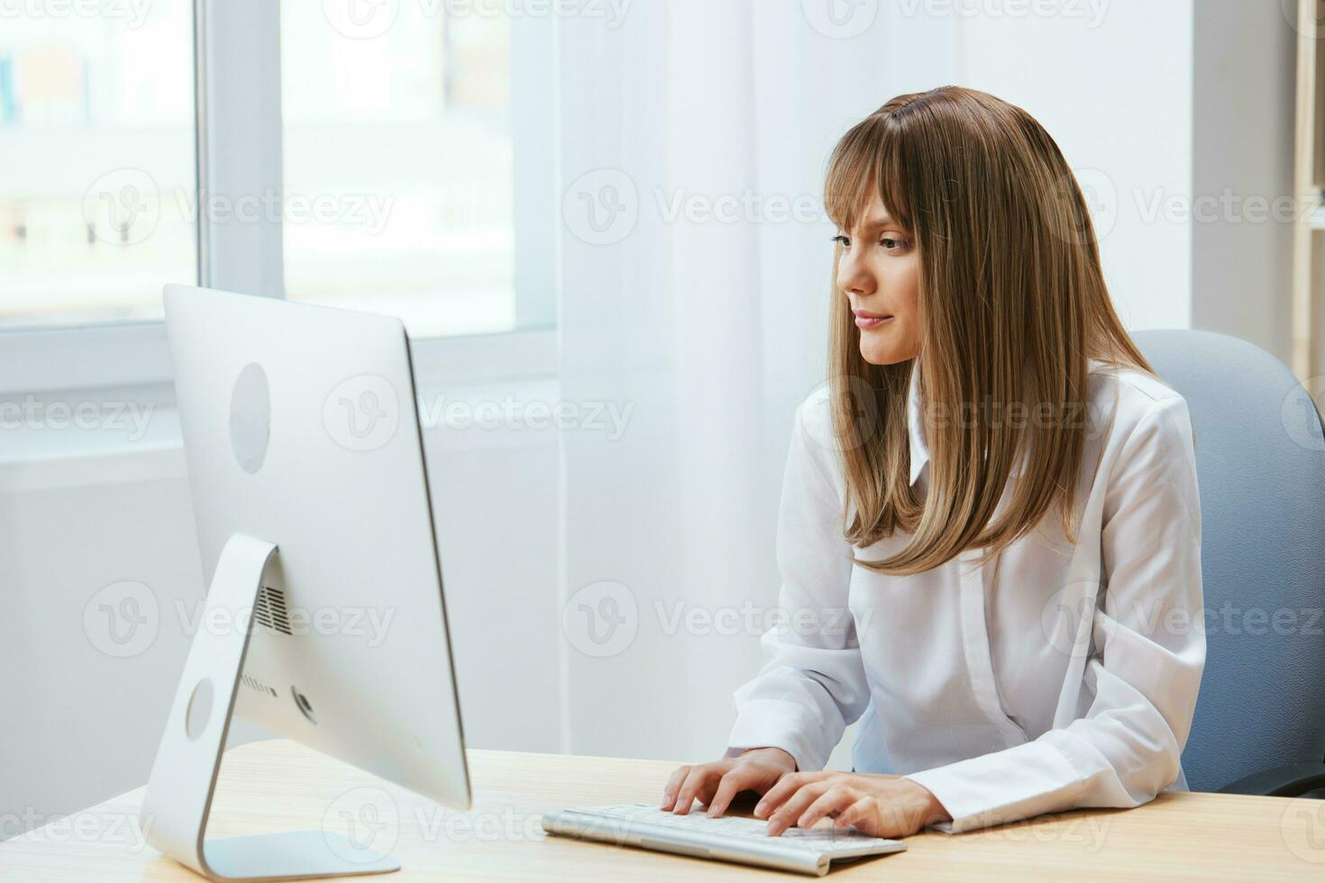 Cheerful happy adorable blonde businesswoman worker freelancer look at screen work on desktop computer online in light modern office. Happy employee writes quarterly report. Copy space, remote job photo