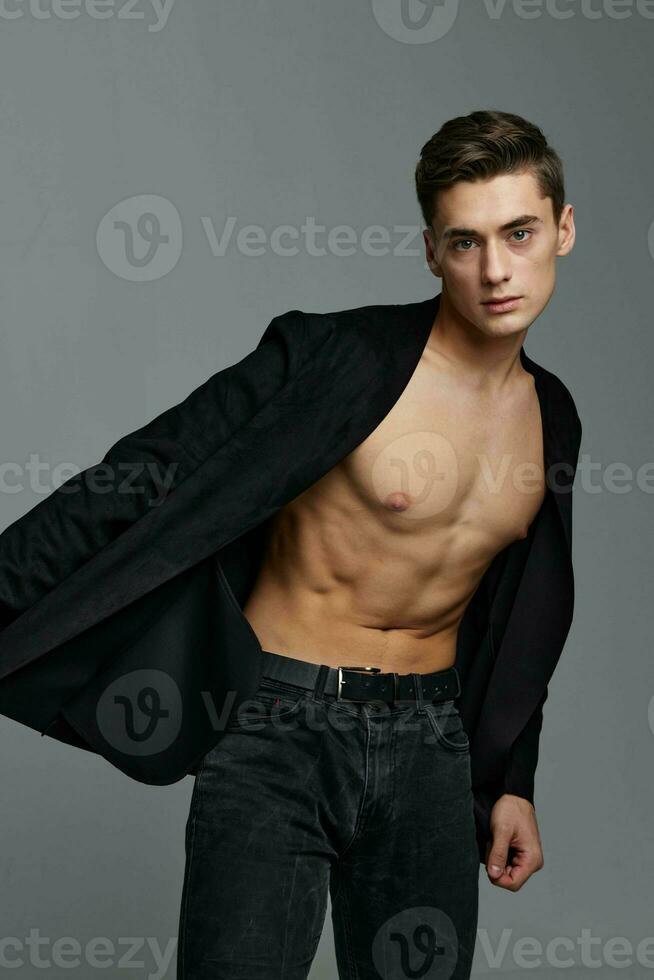 A gentleman in an unbuttoned shirt and trousers on a gray background leaned to the side photo