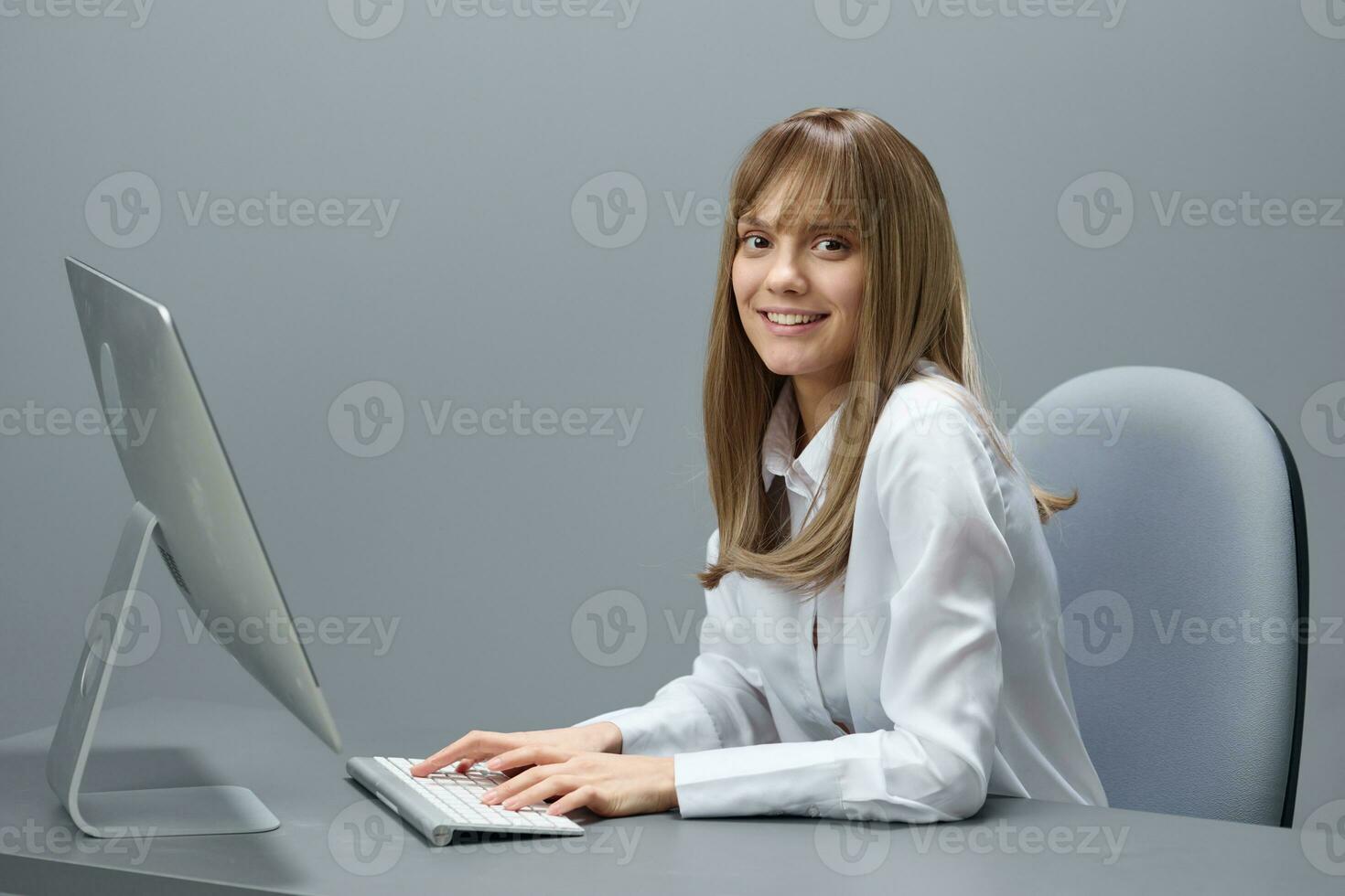 Cute pretty blonde businesswoman freelancer using computer chatting with clients look at camera in gray modern office of support service. Remote Job, Technology Career Profession Concept. Copy space photo