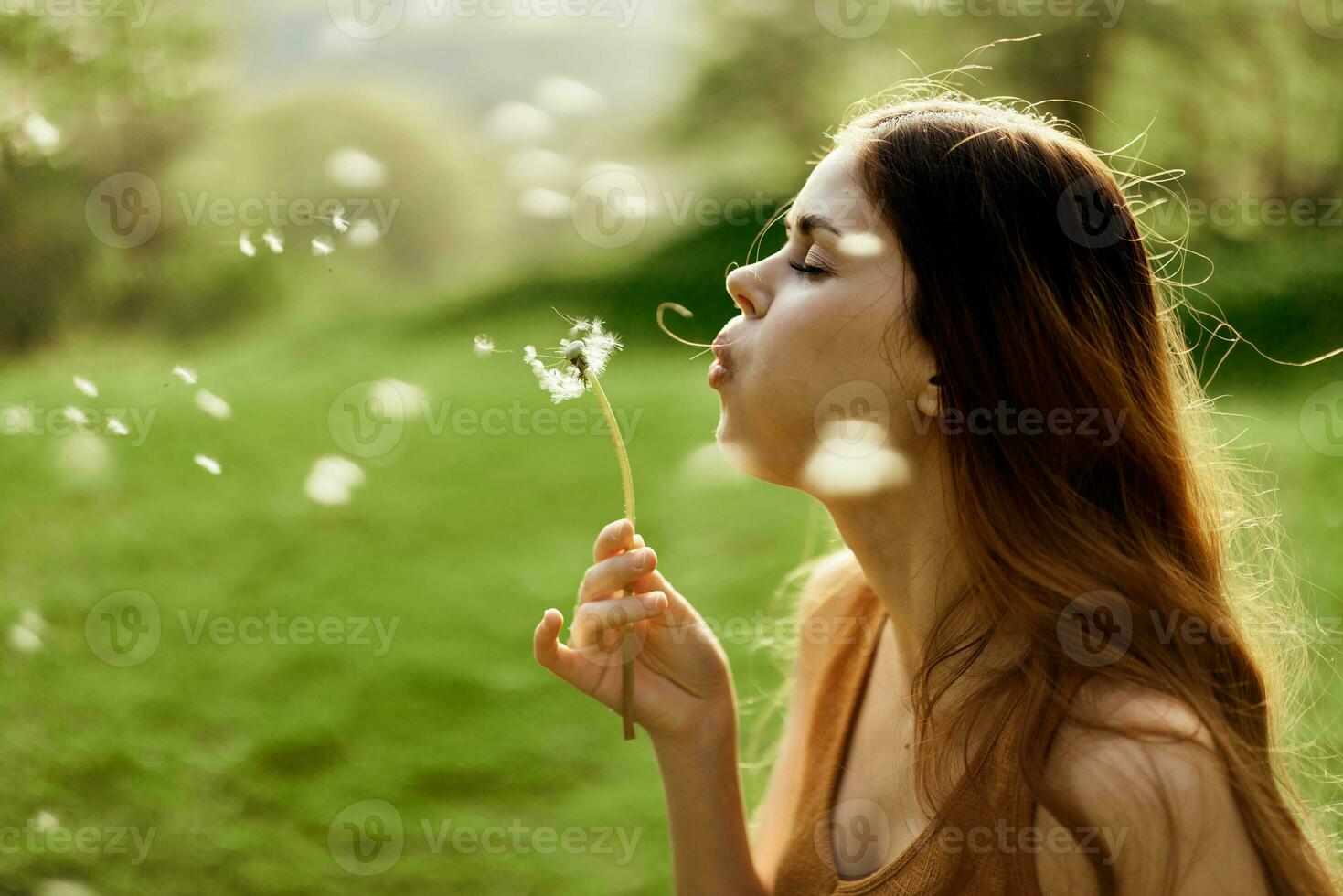 A female freelancer strolls carefree and happily in a green park and blows off a dandelion flower in the sunset light photo