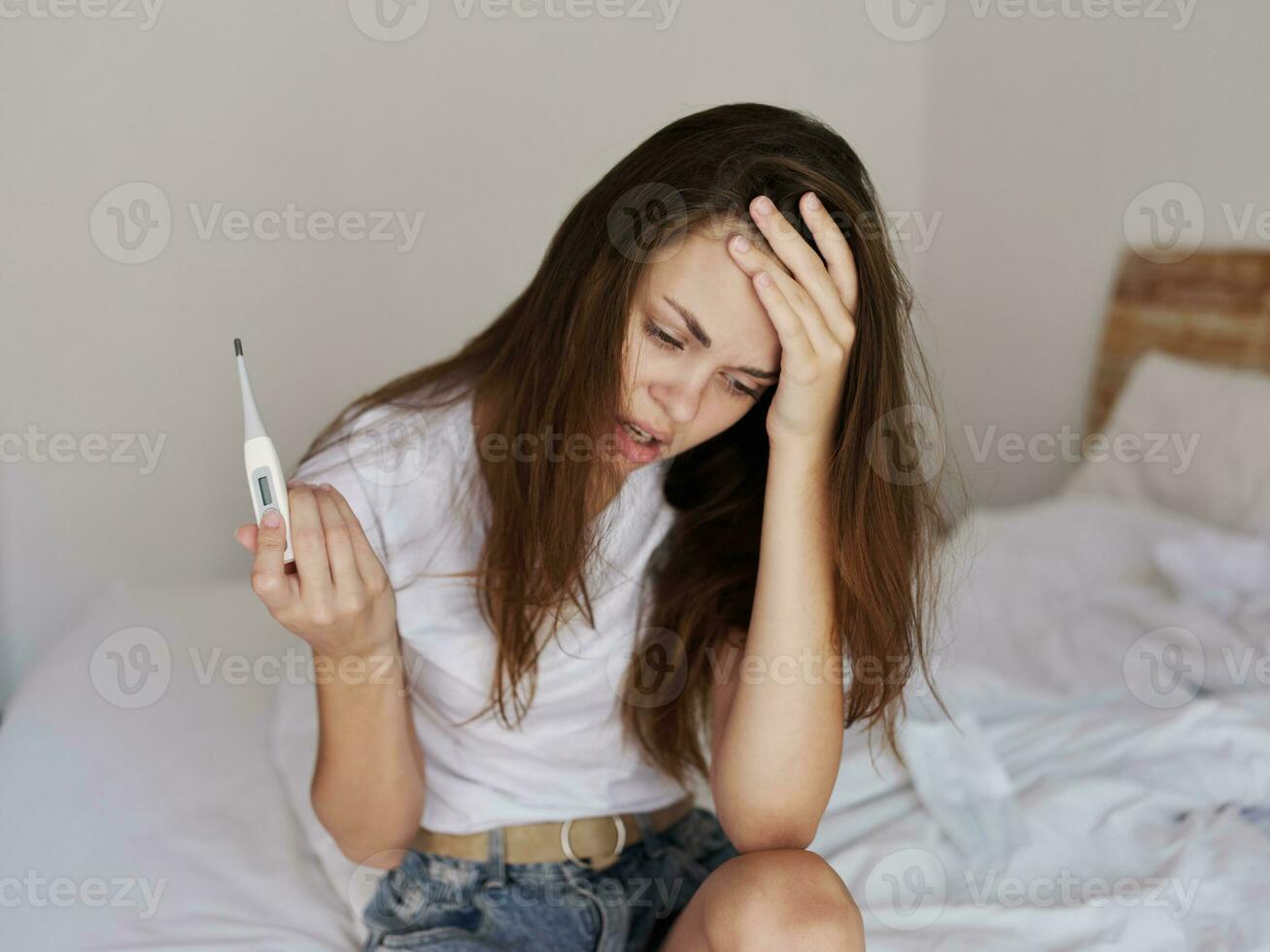 upset woman with a thermometer in her hands sitting on the bed health problems photo