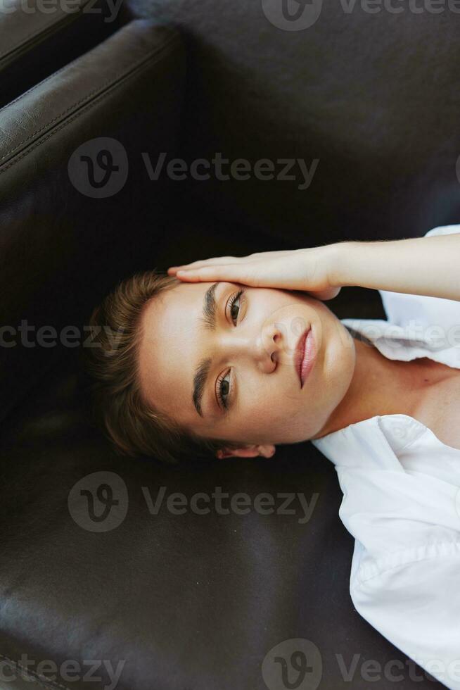 Women lying at home on the couch portrait with a short haircut in a white shirt, smile, depression in teenagers, home holiday photo