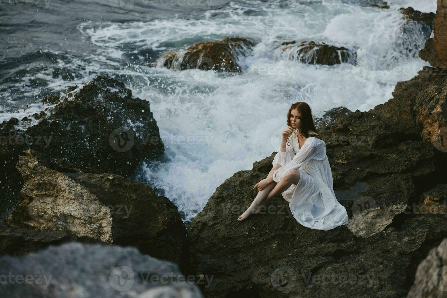 barefoot woman in white dress sits on a stone with wet hair unaltered photo