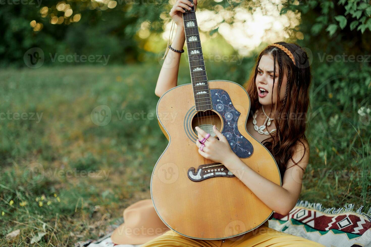 Beautiful woman playing guitar in nature in a hippie summer look, singing songs style of life without worries photo