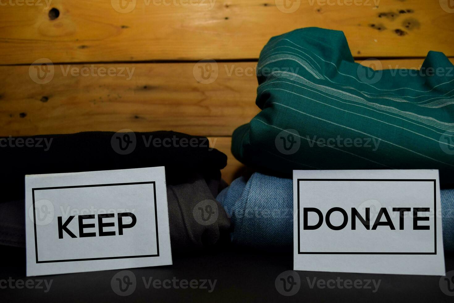 Keep and Donate write on a sticky note between fashion clothes folded and stack isolated on wooden background. photo
