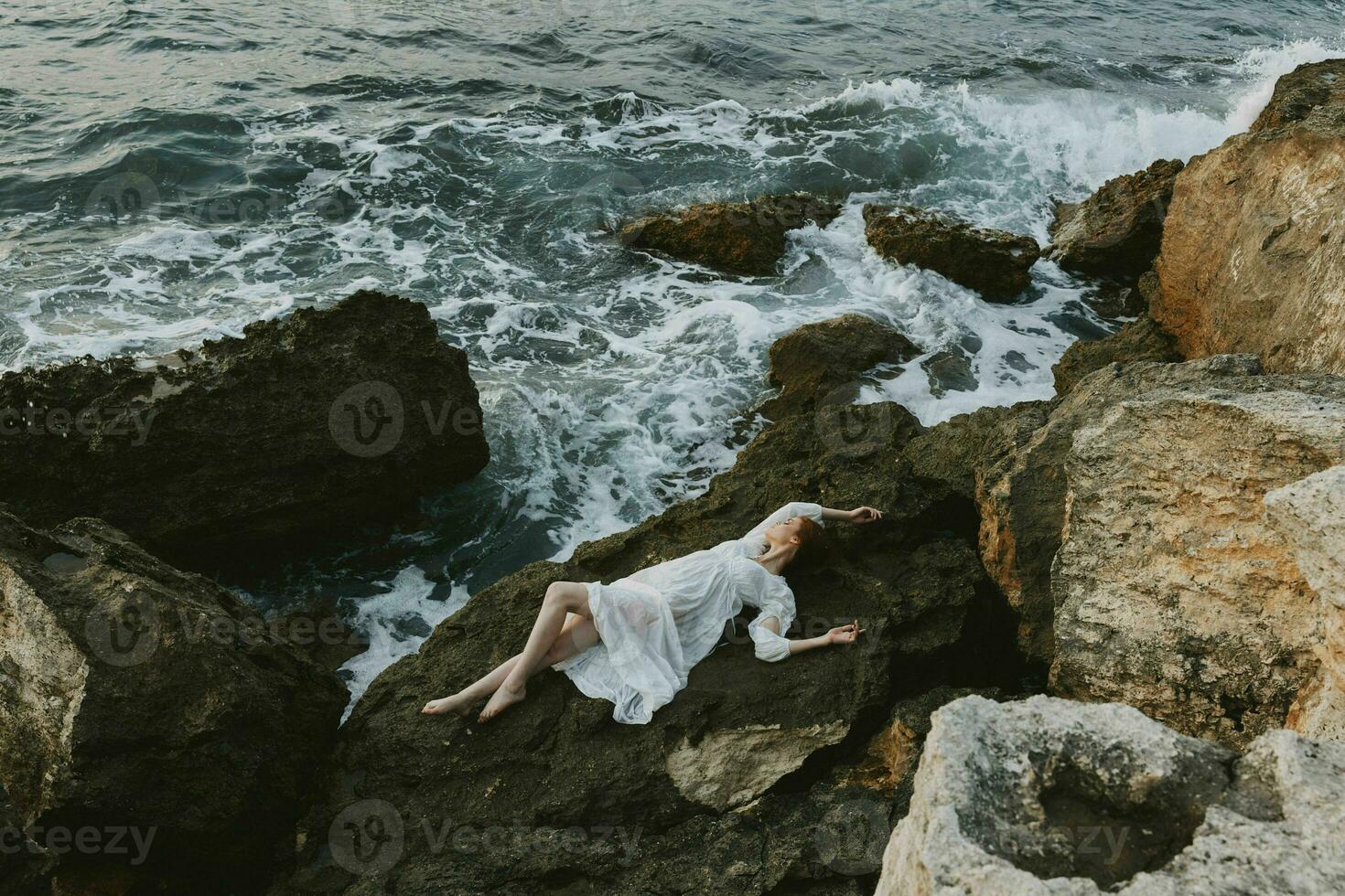 mujer en un blanco vestir acostado en un Roca en un blanco vestir vacaciones concepto foto