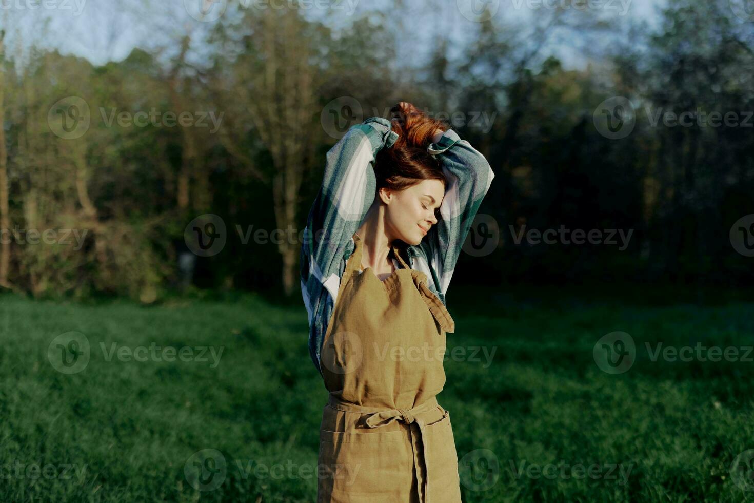 Portrait of a woman with a beautiful smile in her work clothes and apron in nature, enjoying relaxation after work in the sunset sunlight photo