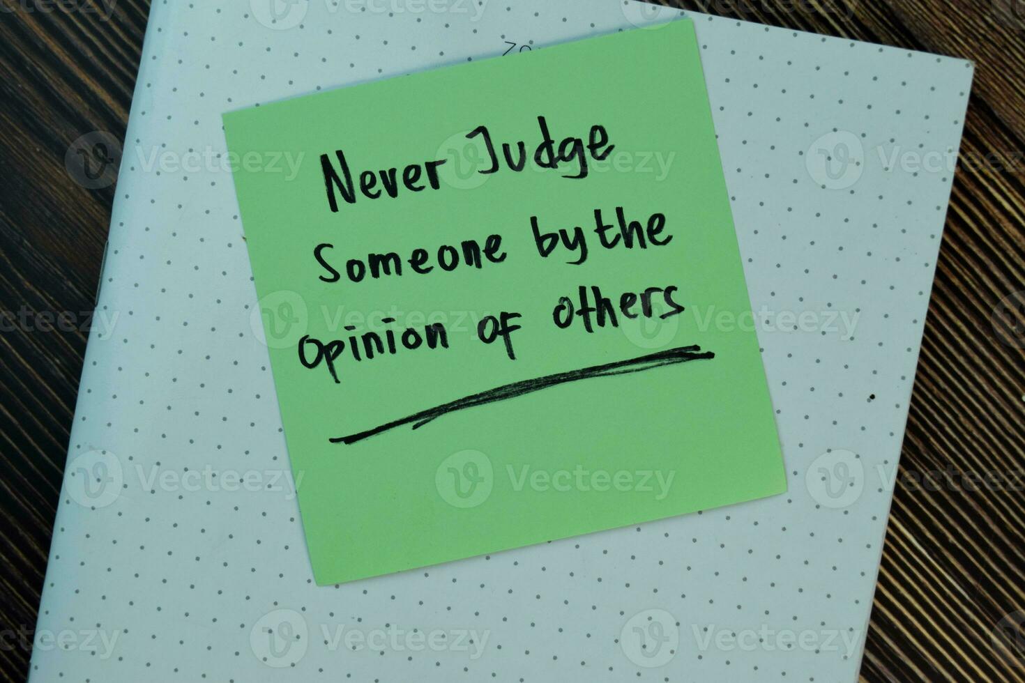 Never judge someone by the opinion of others write on sticky notes isolated on Wooden Table. Motivation concept photo